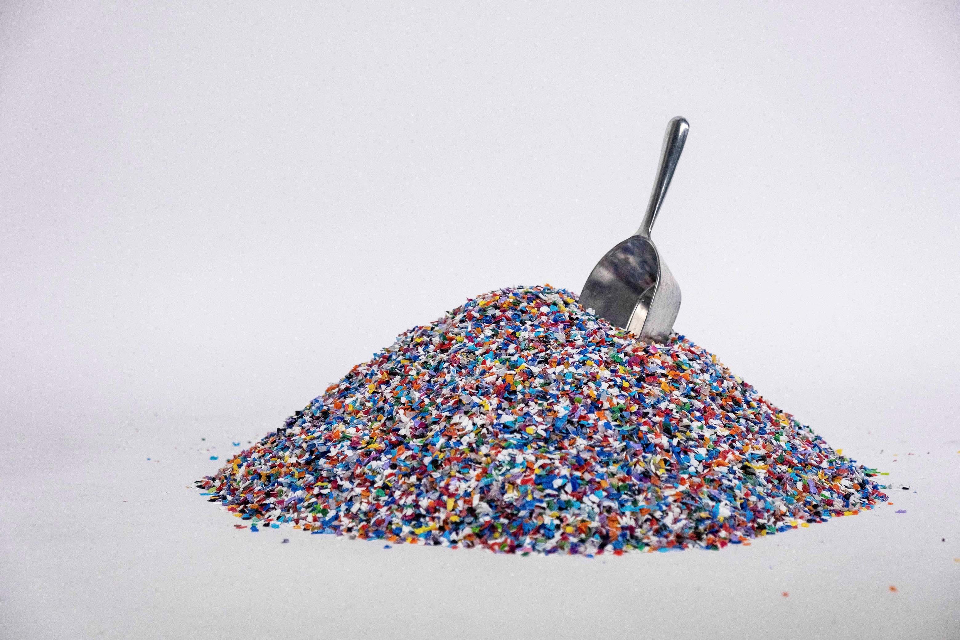 A pile of mixed post-consumer plastic flake with a metal scoop.